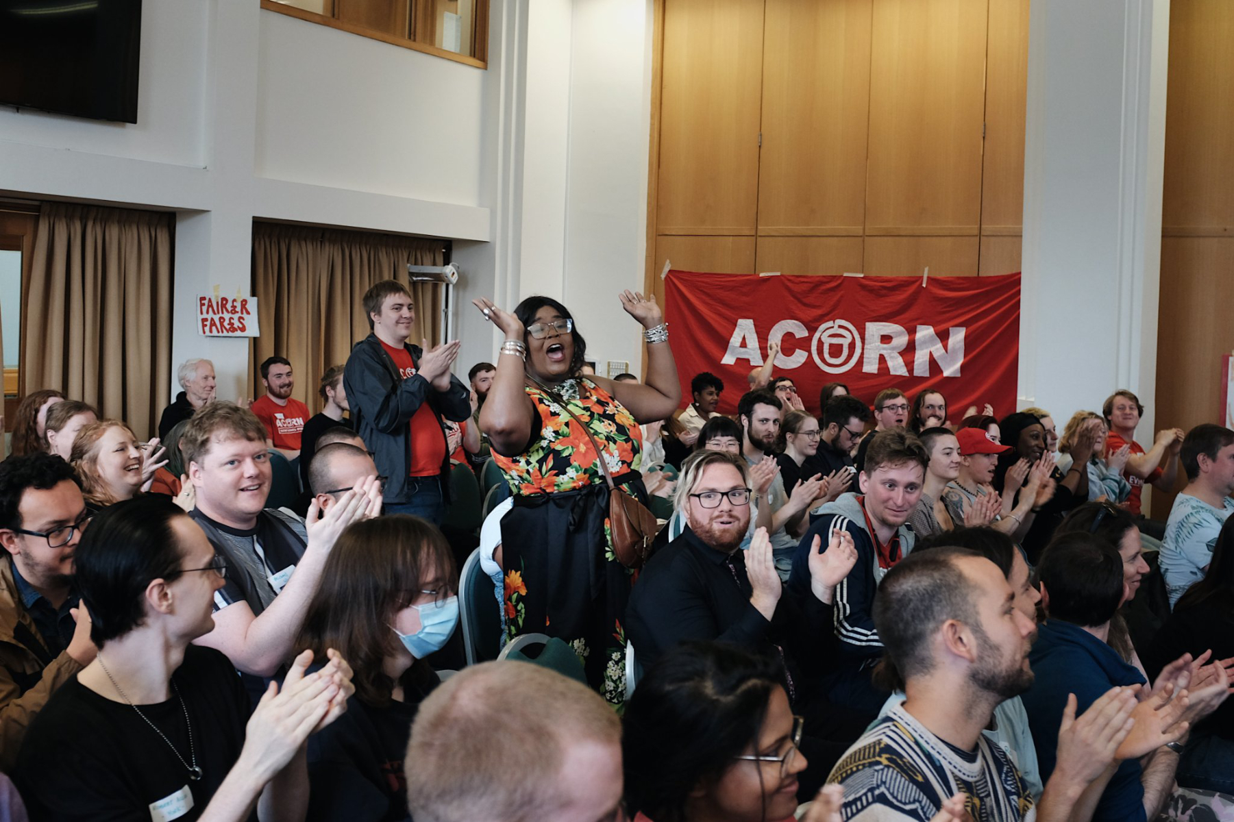 People at a meeting with an ACORN sign. They are cheering and happy.