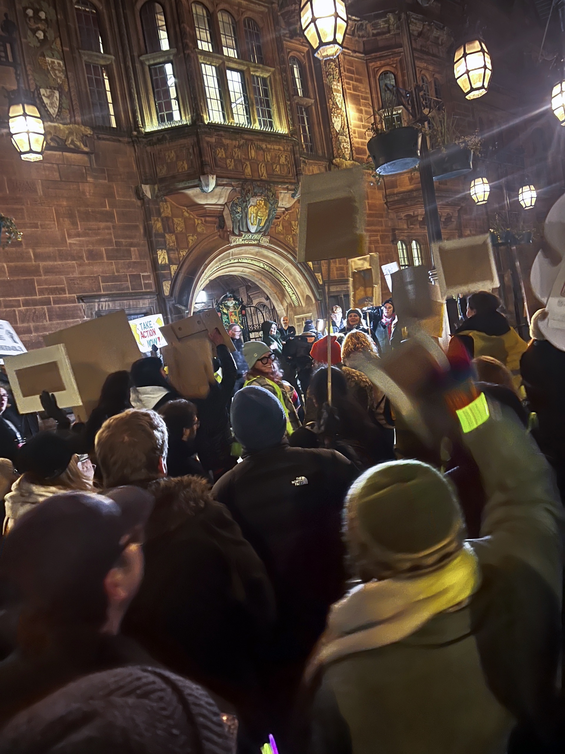 A bunch of people crowded around someone speaking in the street, lit by street lights. Some people are holding placards.