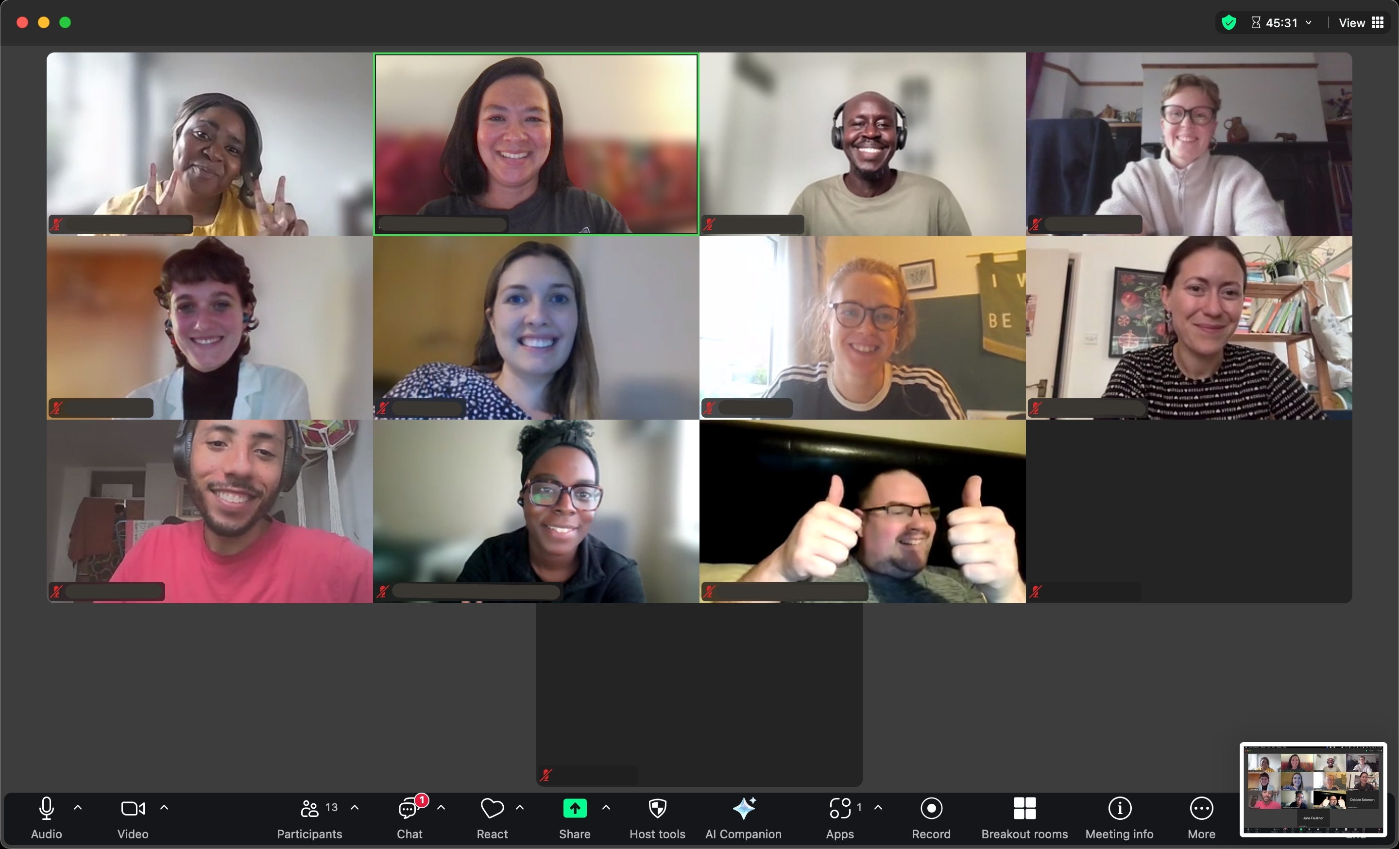 Thirteen people are smiling on a Zoom call, each in their individual; rectangle screens. Two have their video off. One person is holding their thumbs up and another is holding up two peace signs.