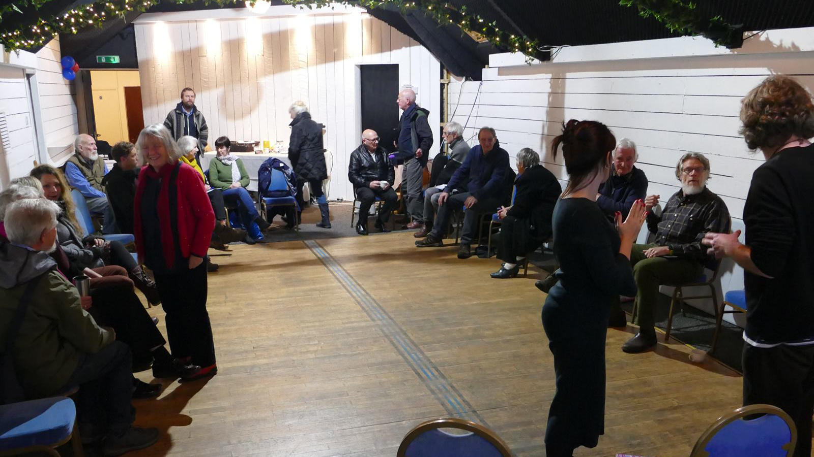 An image of people sitting in a circle with a woman at the front teaching.
