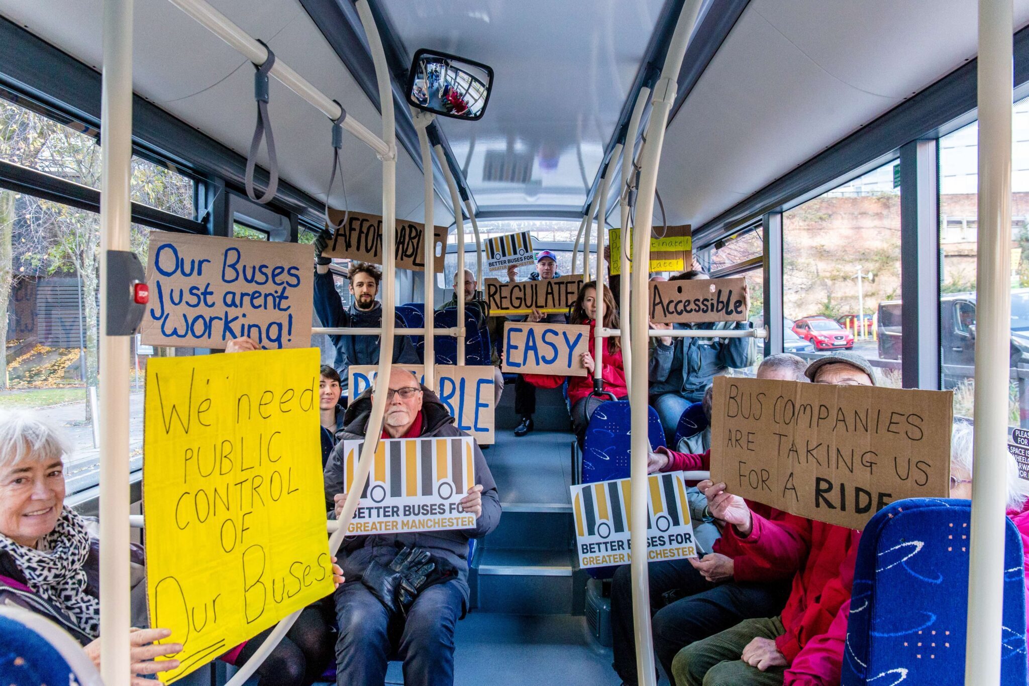 People sitting on a bus with placards calling for better buses in Greater Manchester.