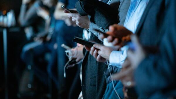 A side angle perspective of a row of people, focused on their hands, each of them using mobile phones.