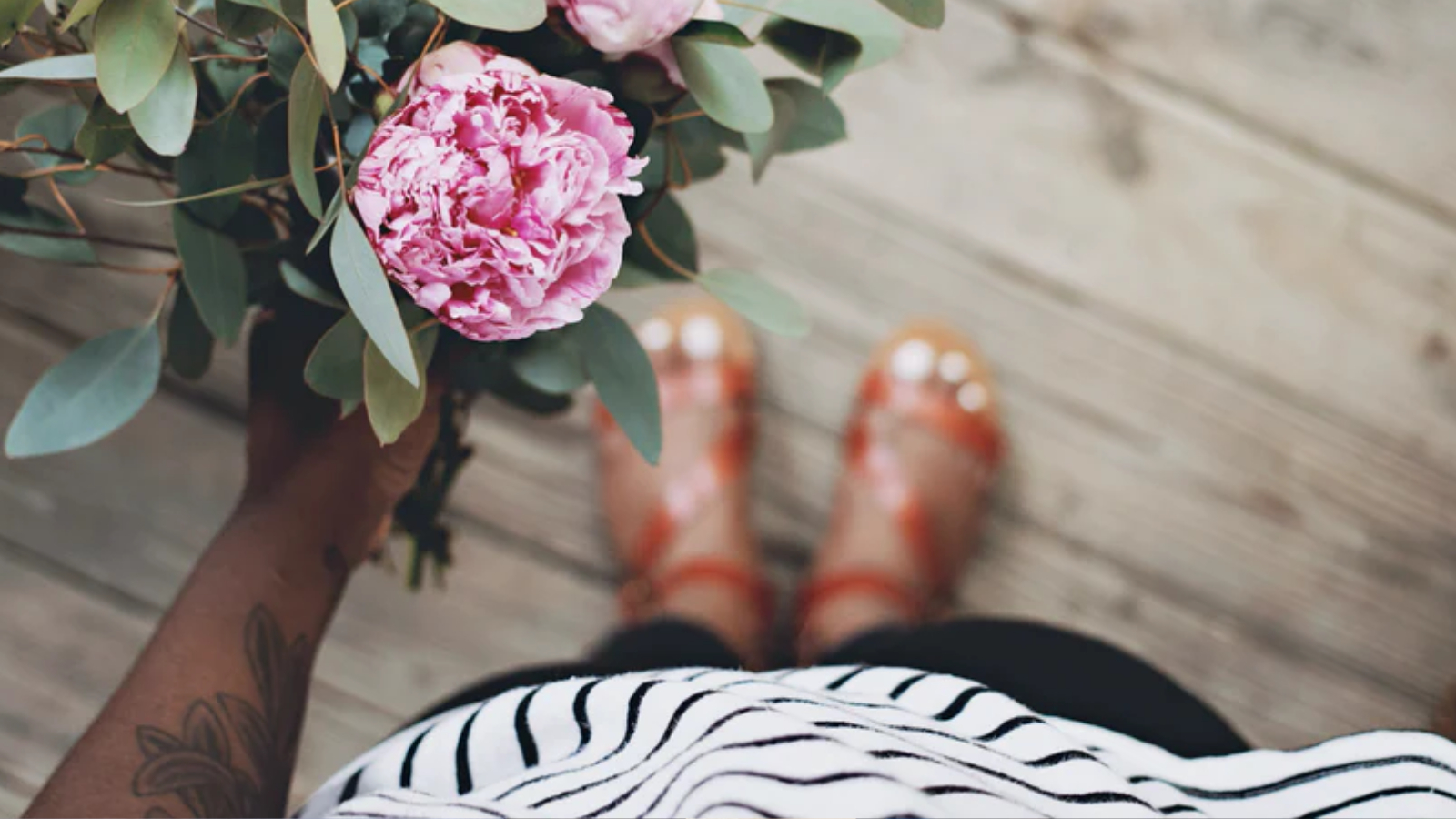 An image of a person holding a pink flower. You can see her hand and feet.