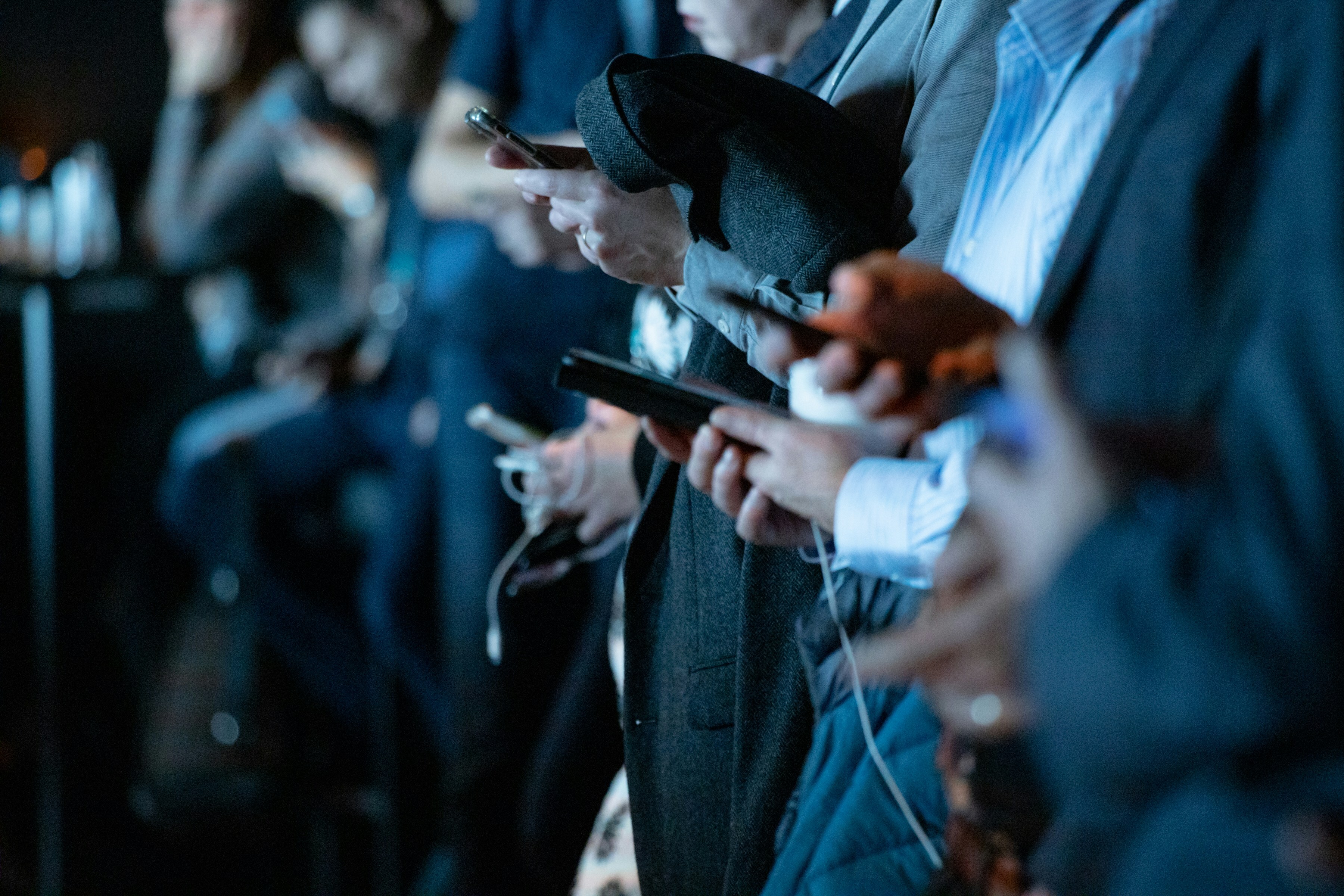 A side angle perspective of a row of people, focused on their hands, each of them using mobile phones.