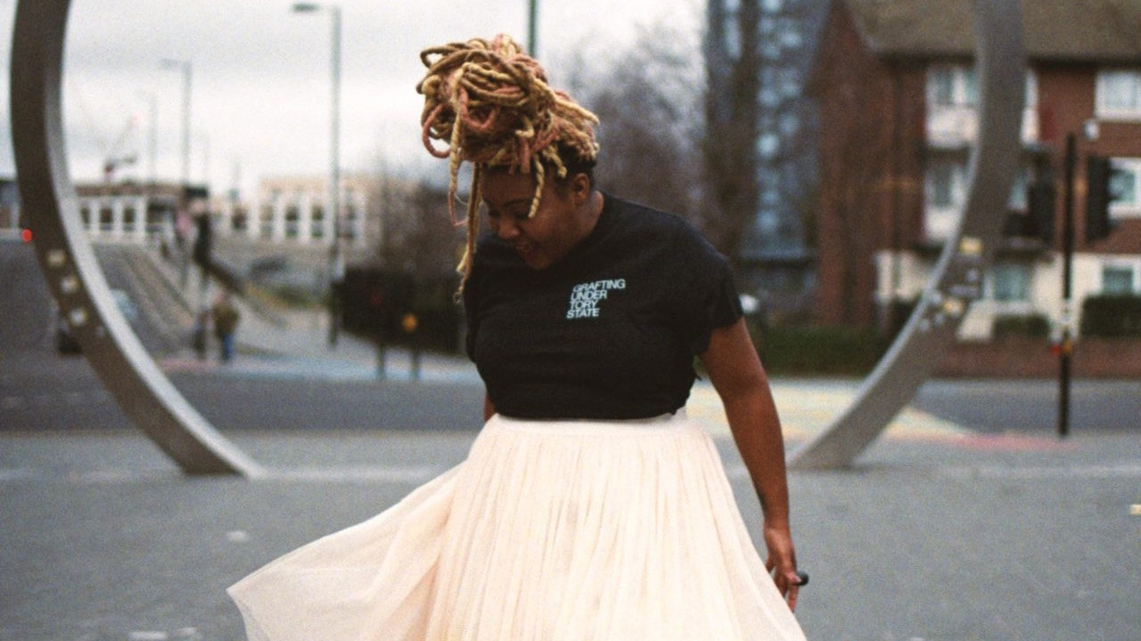 Janine Francois standing in the street looking down smiling as there skirt is blowing in the wind.